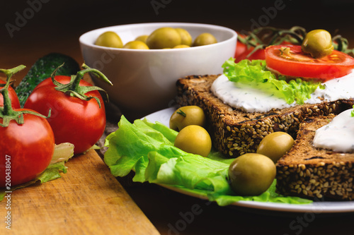 Sandwiches with healthy rye bread, cheese cream, tomatoes, green olives and lettuce on table. Healthy vegetarian food concept