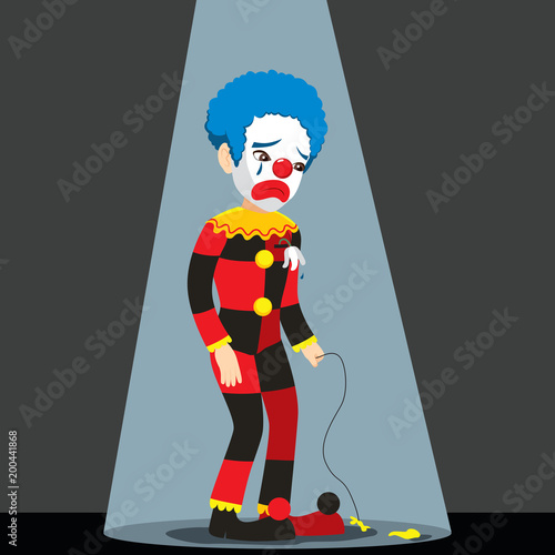 Sad clown standing under spotlight with punctured balloon crying