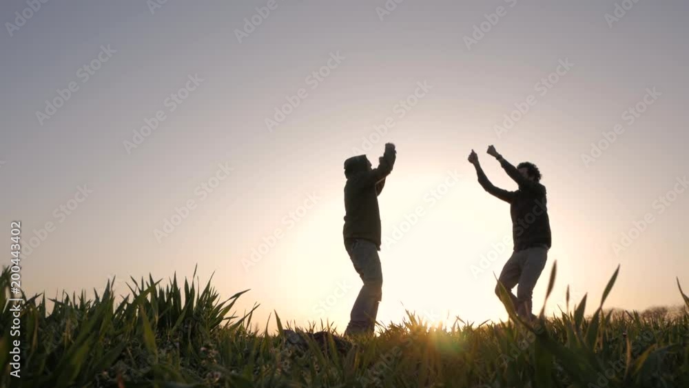 silhouette of two young peoples running, jumping and having fun in spring fields, sunset background silhouette of two young peoples running, jumping and having fun in spring fields, sunset background