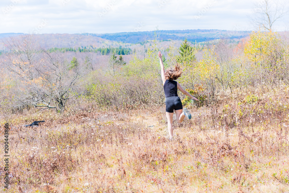 Young athletic, fit, free happy woman running jogging jumping in autumn, fall, summer meadow field path hike in mid-air, muscles