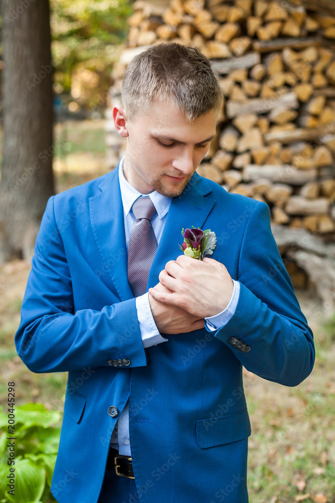 Groom correcting boutonniere near wooden logs Groom correcting boutonniere near wooden logs