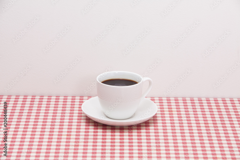 A cup of coffee on red and white checkered table 