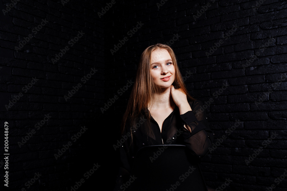 Studio shot of brunette girl in black blouse with bra and shorts against black brick wall. Studio shot of brunette girl in black blouse with bra and shorts against black brick wall.