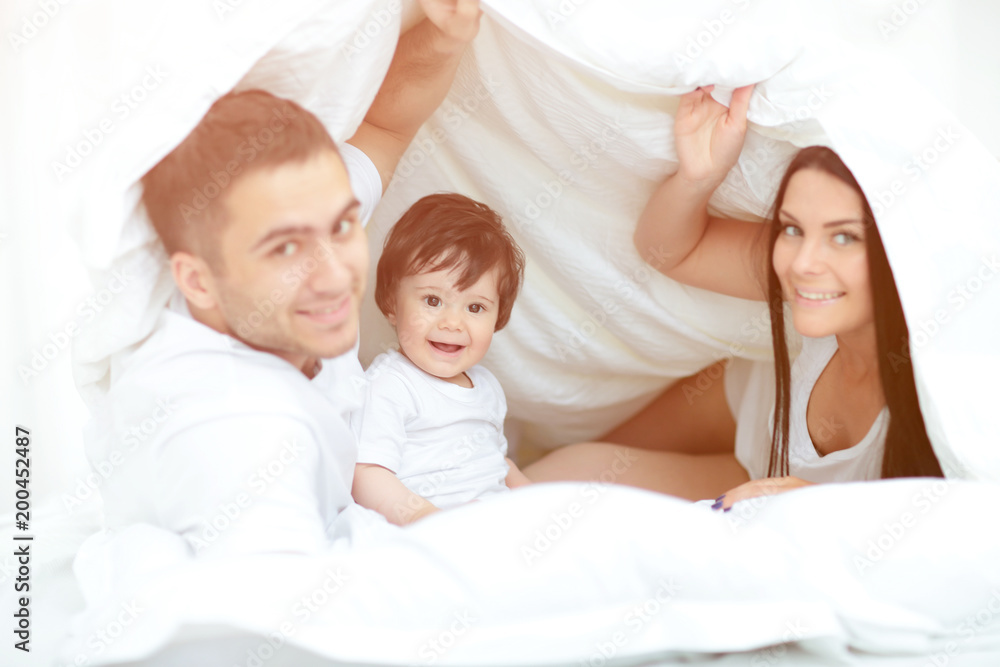 Happy family posing under a duvet while looking at the camera Happy family posing under a duvet while looking at the camera