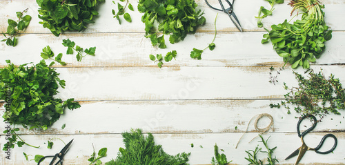 Flat-lay of bunches of various fresh green herbs. Parsley, mint, dill, cilantro, rosemary, thyme over wooden background, top view, copy space, wide composition. Healthy vegan cooking concept