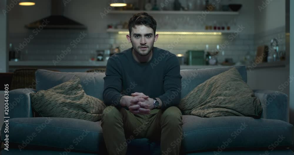 Young man sitting on the edge of a couch watching a scary movie. Young man sitting on the edge of a couch watching a scary movie.