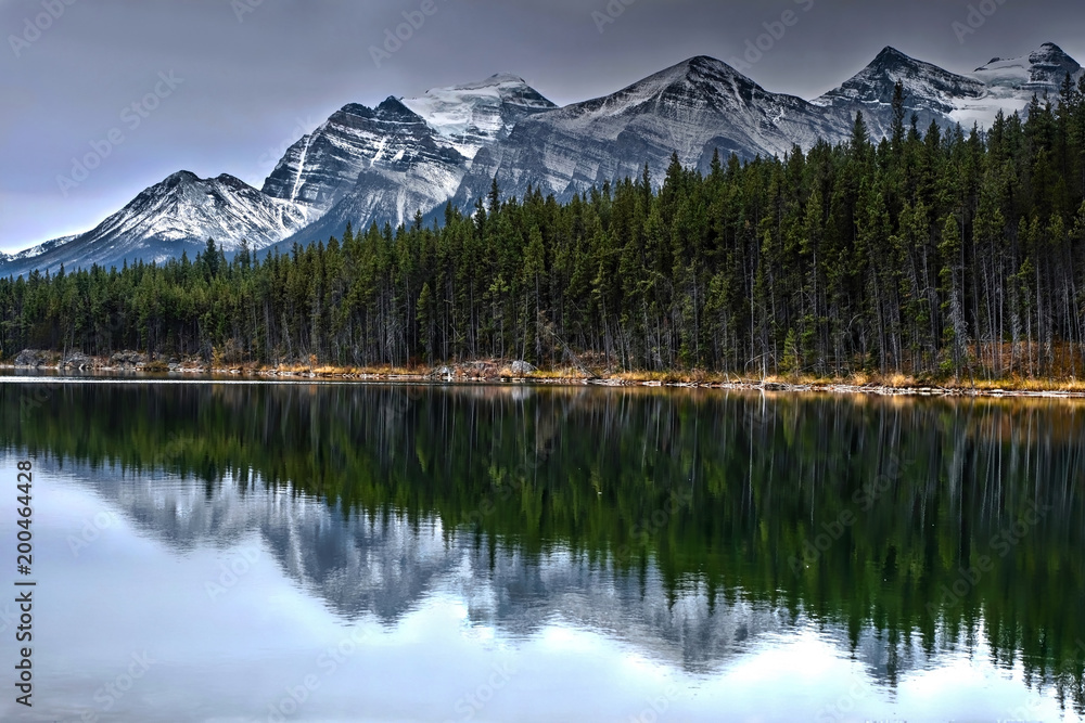 Mountain peaks covered with snow,  forest and reflections in calm lake. Herbert lake near Banff in Banff National Park. Canadian Rockies.  Alberta. Canada.