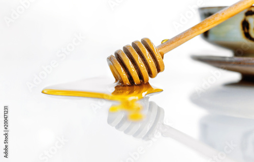 Golden sweet honey with a wooden honey dipper on the white ceramic background.
