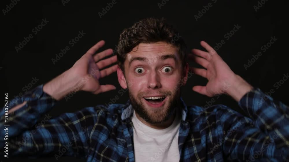 An attractive young man showing delight by touching the back of his head against a black background. Close-up Shot An attractive young man showing delight by touching the back of his head against a black background. Close-up Shot