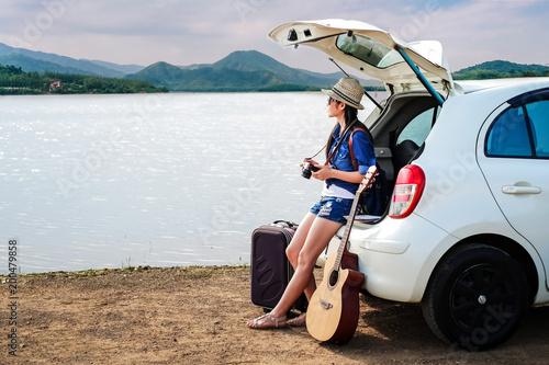 woman traveler sitting on hatchback of car and looking to local map near the lake during holiday background is the mountain.Young lady tourist enjoying for view of nature on vacation. 