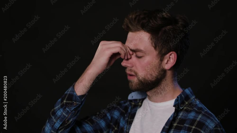 A young man immitating a headache against a black background. Close-up Shot A young man immitating a headache against a black background. Close-up Shot