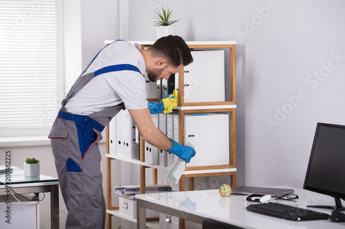 Man Cleaning Desk In Office