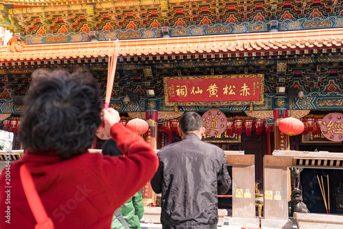 Hong Kong people with incense pay respect and praying to god with the name of the temple Wong Tai Sin Temple in the background.