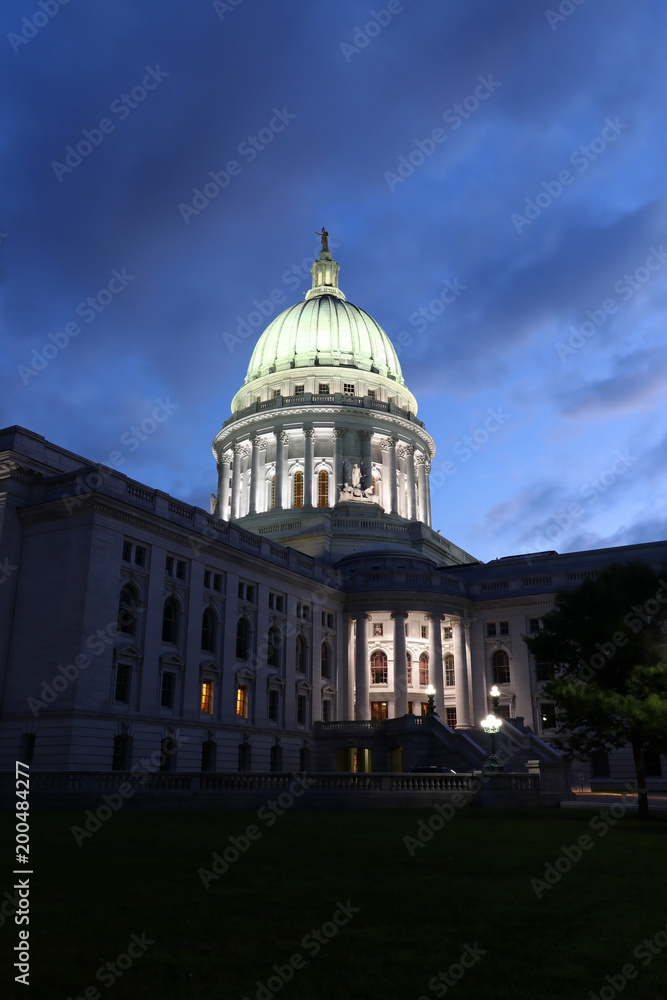 Wisconsin state capitol building at dusk. Night scene with illuminated entrance and glowing at the dark dome against dark blue sky. City of Madison, Wisconsin, Midwest USA. Vertical composition.
