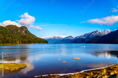Fototapeta Naklejka Na Ścianę i Meble -  Fishing Boat heading up Pitt Lake with the Snow Capped Peaks of the Golden Ears, Tingle Peak and other Mountain Peaks of the Coast Mountain Range in the Fraser Valley of British Columbia, Canada