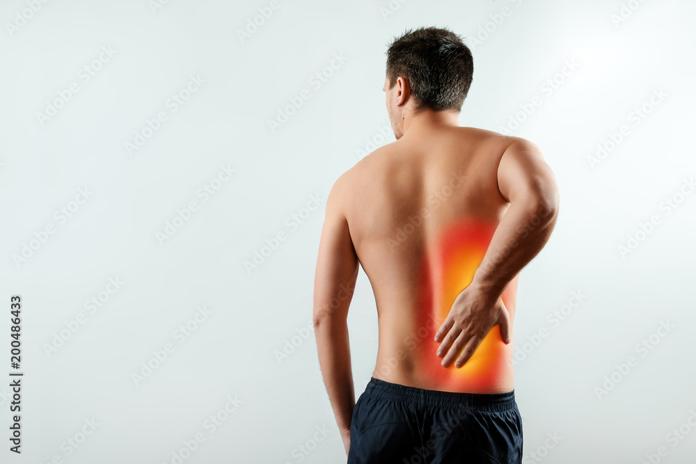 The man holds his hands behind his back, pain in the kidneys, pain in his back. Light background. The concept of medicine. The man holds his hands behind his back, pain in the kidneys, pain in his back. Light background. The concept of medicine.