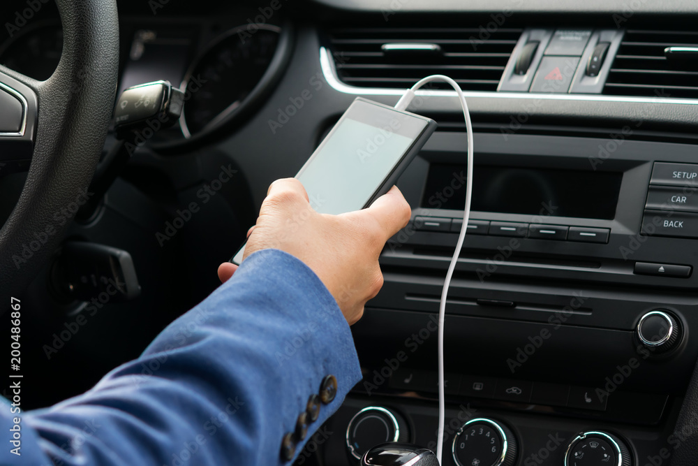 the driver of the vehicle, holds in his hand the phone connected by a white wire, to the car's music system