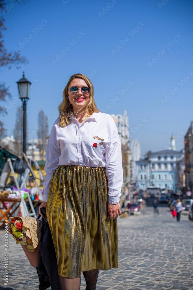A woman of plus size, American or European appearance walks in the city enjoying life. A young lady with excess weight, stylishly dressed in jacket at the center of the city. Natural beauty 