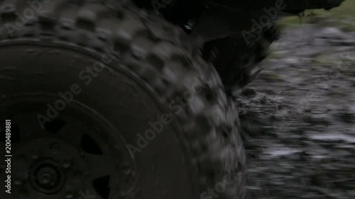 Close up, slow motion shot of off-road vehicles front entering very muddy terrain, splashing mud around and driving away.