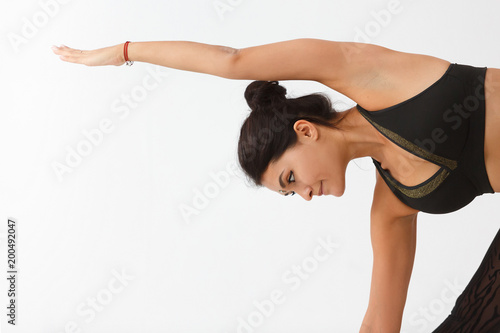 Sporty beautiful young woman practicing yoga, doing Revolved Triangle Pose, Parivrrta Trikonasana, working out wearing black sportswear, white studio, full length, white background