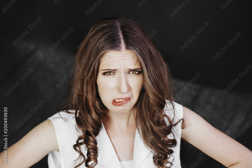 Woman with uncombed hair make a grimace in white shirt stand studio shoot on dark background.