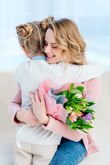 happy mother hugging daughter and holding bouquet on happy mothers day