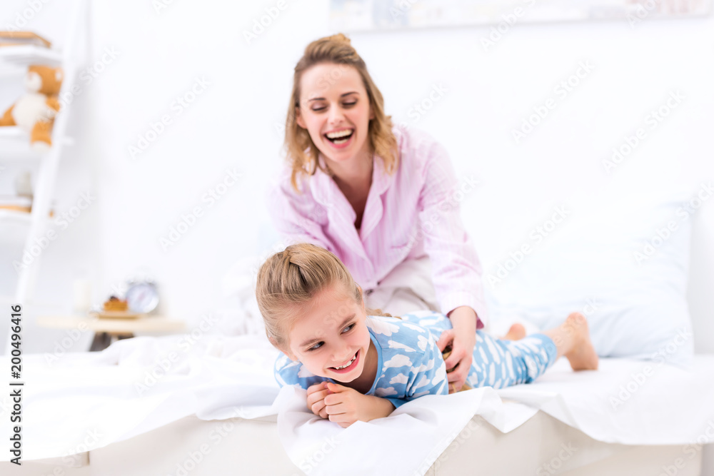 smiling mother tickling daughter on bed at home smiling mother tickling daughter on bed at home