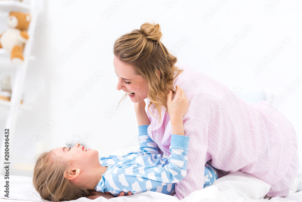 happy mother and daughter having fun and playing on bed at home happy mother and daughter having fun and playing on bed at home