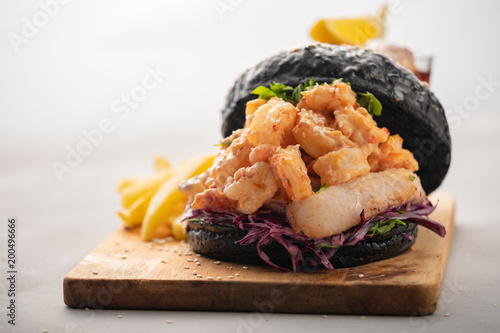 Black burger with fish and shrimps. Fishburger with prawns over light background