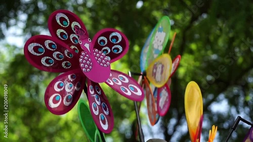 Colorful pinwheel, wind spinner toys - close up. Selective focus on the spinning purple wind mill, weather vane, in the foreground. Out of focus green trees in the background. photo