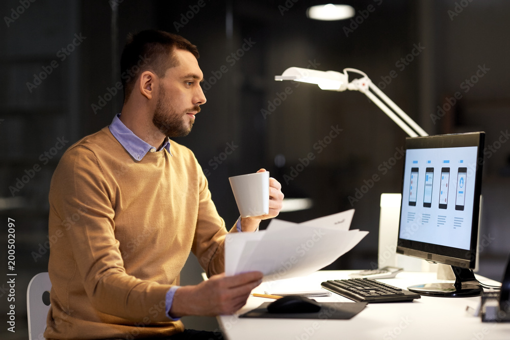 Fototapeta premium business, software development, deadline and technology concept - man with papers, coffee and user interface mockup on computer screen working at night office