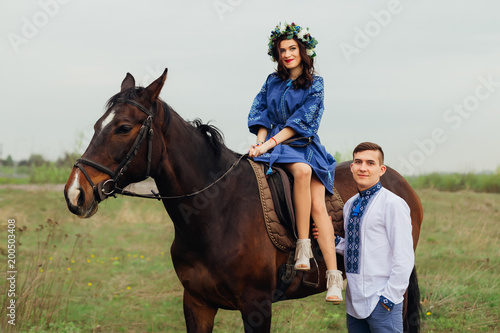 the girl who elegantly sits in the saddle on a horse and her boyfriend who stands next to her and they look at the camera lens
