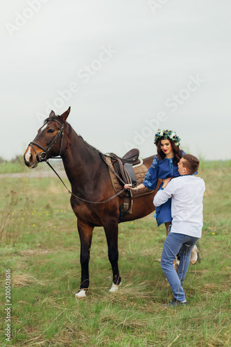 The guy helps his girlfriend get off the horse on the background of the meadow