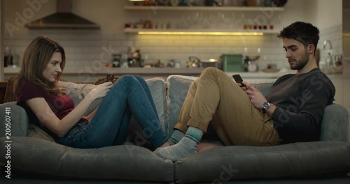 Man and woman ignore each other on the sofa while using their smartphones for social media. photo