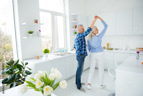Side view full size portrait of lovely stylish attractive creative couple in casual outfit dancing in pair in the kitchen, enjoying morning, spending time together, woman making turn around