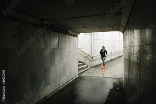 Urban sporty woman running in the city. Female athlete training outside in rainy winter.