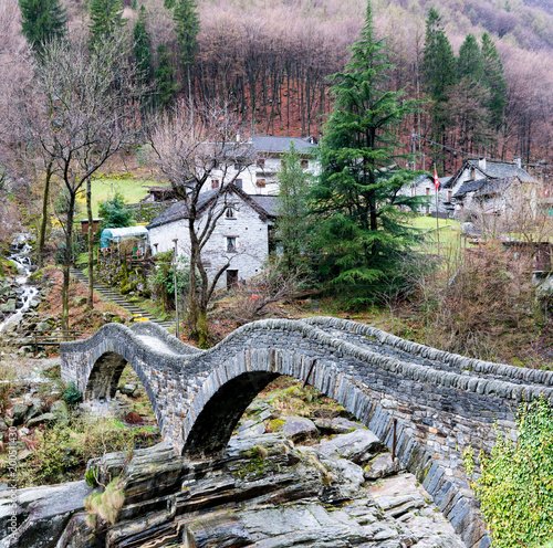 view of the old Roman stone bridge with two arches near the village of Lavertezzo in the Swiss Alps