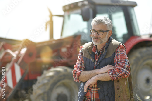 Photographie Farmer standing by tractor outside the barn