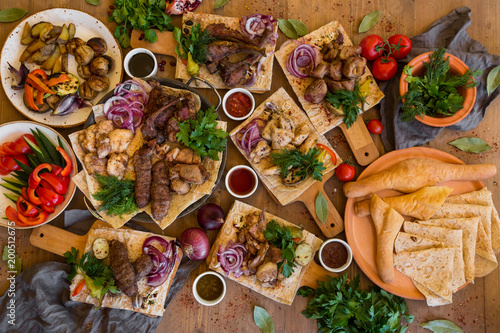 Outdoors Food Concept. Appetizing barbecued steak, sausages and grilled vegetables on a wooden picnic table.