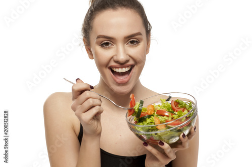 Young beautiful woman eating salad on white background