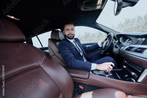 View from the side confident businessman sits at the wheel of a 