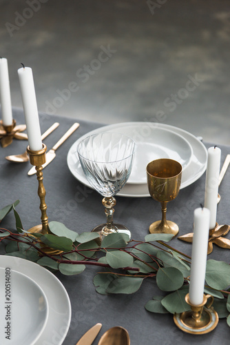 close up view of rustic table setting with wine glasses, eucalyptus, old fashioned cutlery, candles in candle holders and empty plates photo