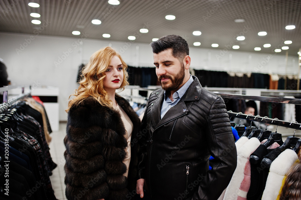 Elegance blonde girl in fur coat and stylish turkish man at the store of fur coats and leather jackets.