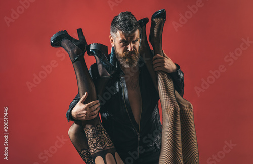 Womanizer. Bearded brutal man with female legs in sexy pantyhose. Seductive sensual relationship. Passion and polygamy. Fashion and beauty. Pimp and model agent. Man and two women, seductive legs photo