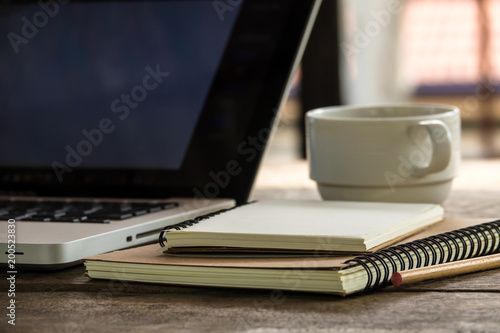 Top view of blank notebook with white coffee, laptop and with natural light on wooden table.