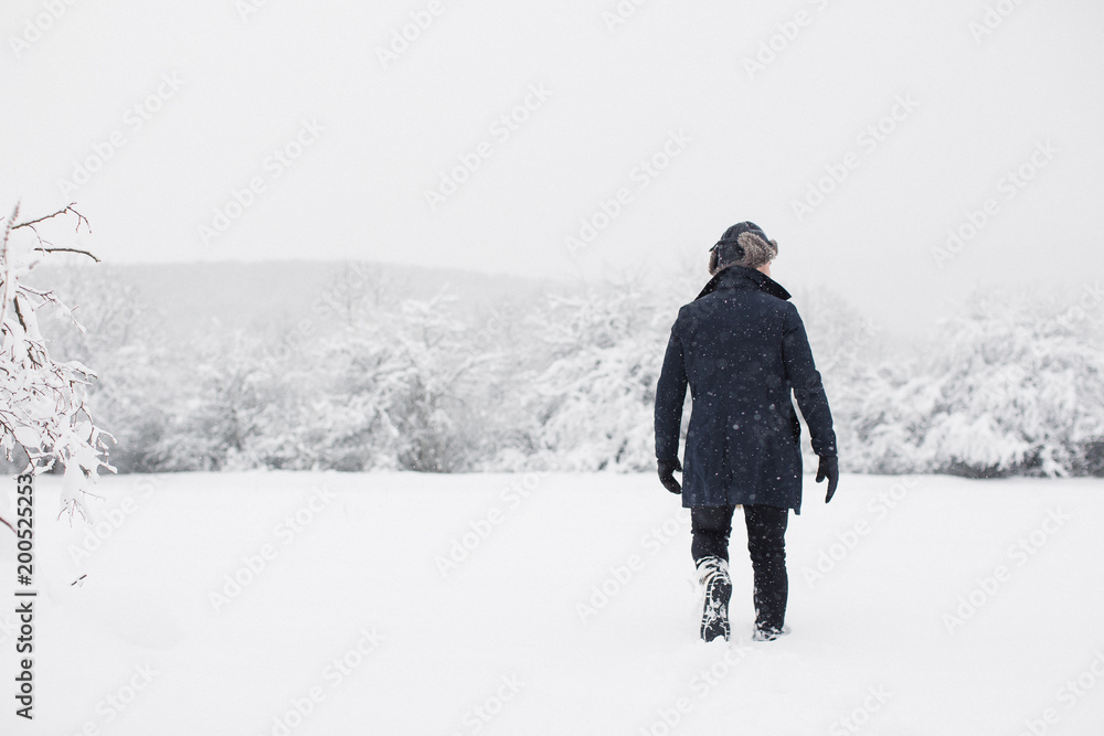 The young man walking in the snow outdoor and looking aside