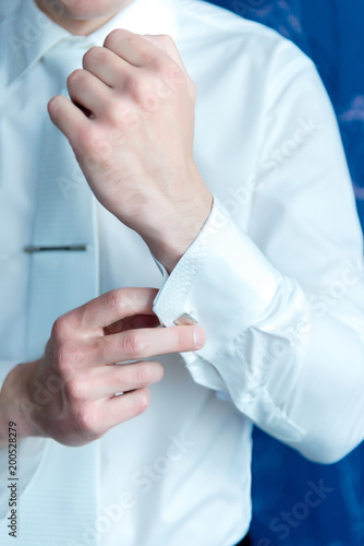 The man in the white shirt adjusts his cufflinks on the sleeves. Elegant fashion businessman fixing his cufflinks, closeup