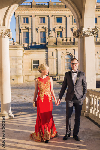 The happy young beautiful, elegant couple walking by the palace and holding hands