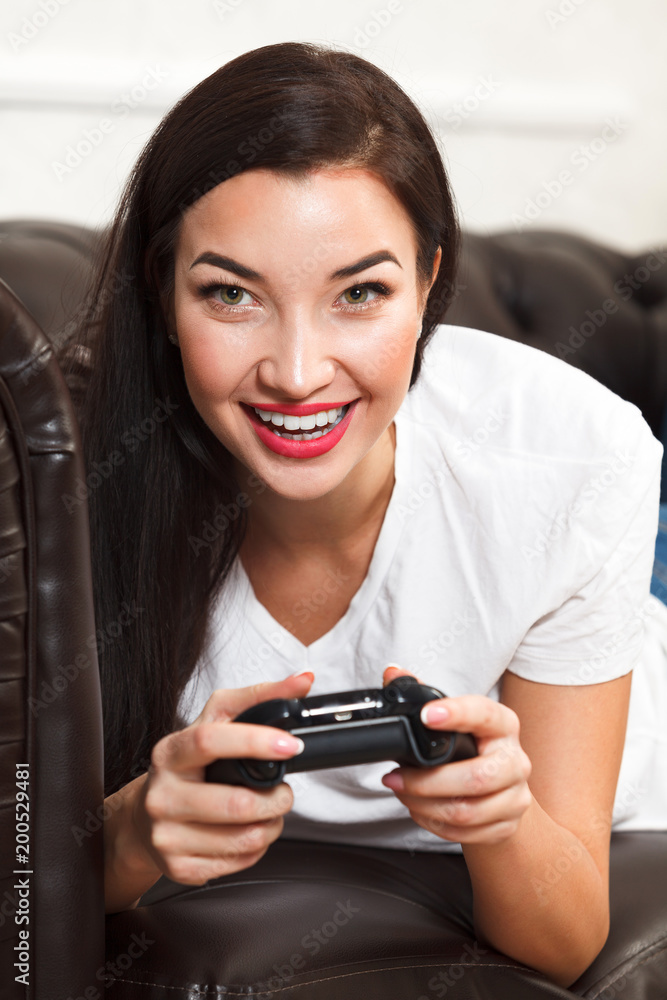 Woman gamer lies on brown leather sofa and plays a video game Woman gamer lies on brown leather sofa and plays a video game