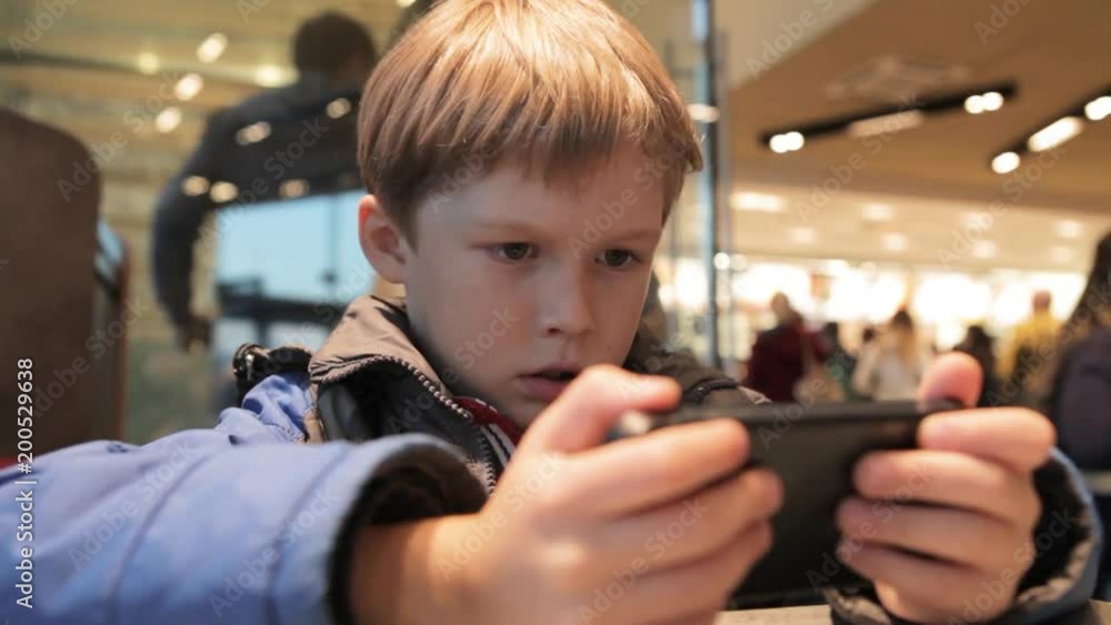 custom made wallpaper toronto digitalLittle boy is playing with phone in cafe. Blonde boy with a phone.
